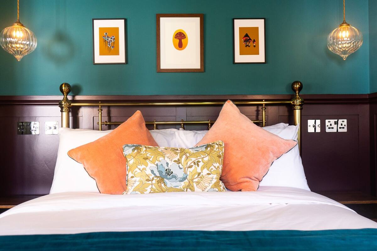A neatly made bed with white linens and decorative pillows, a wooden headboard, and two wall-mounted light fixtures.