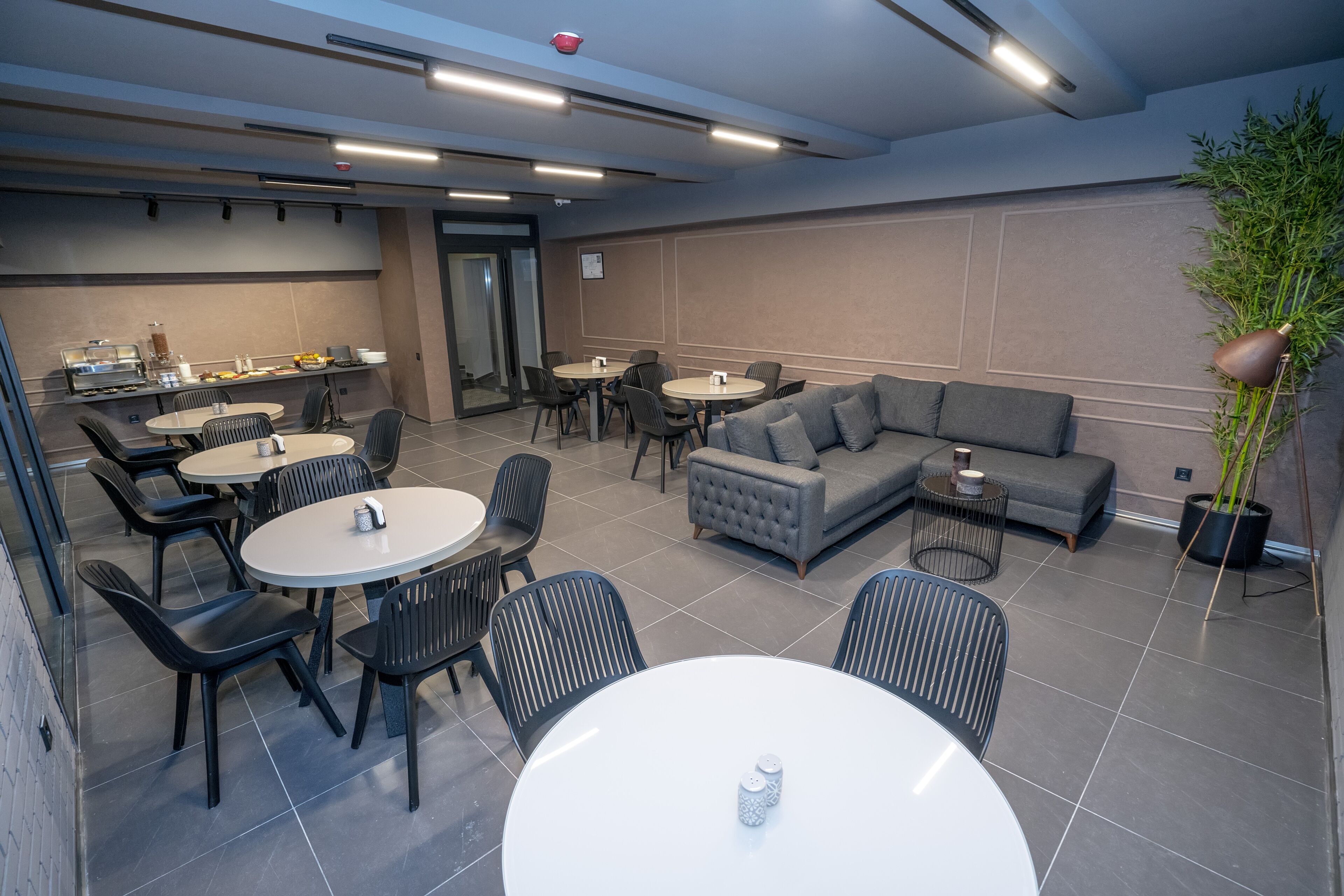 A modern lounge area with round tables, black chairs, a grey sofa, and a small side table.