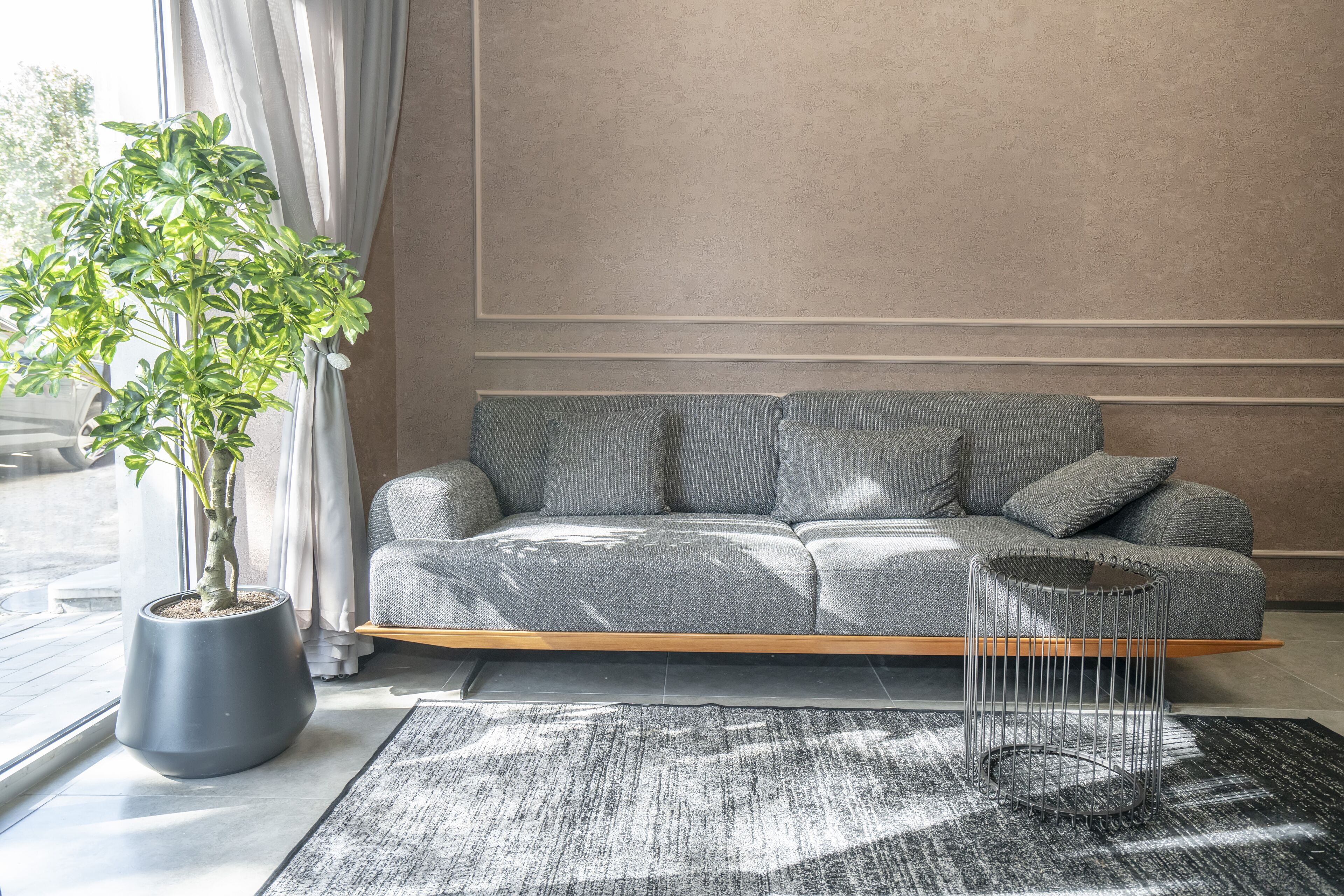 A modern living room with a grey sofa, a potted plant, and a metal side table.