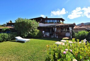 Relax in a serene outdoor space with a covered patio, seating, and dining area surrounded by lush greenery and a well-maintained lawn.