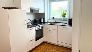 Une cuisine moderne avec des meubles blancs, une cuisinière, un four et une fenêtre donnant sur l’extérieur.
