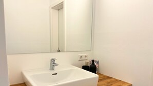 Une salle de bain avec un lavabo blanc, un plan de toilette en bois et un miroir.