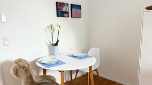 Un coin repas avec une table ronde blanche, deux chaises, un vase de fleurs et deux tableaux abstraits accrochés au mur.