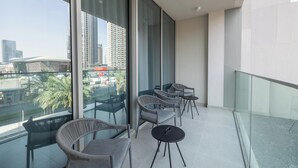 Ein Balkon mit modernen Korbmöbeln, Tischen, großen Fenstern mit Blick auf die Stadt und einem Glasgeländer.