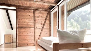 A wooden bunk bed with a white pillow, a wooden wardrobe, and a large window with a view of trees. - *Schwarzwald-Haus mit Sauna* (Elzach)