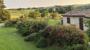 A rustic stone building with a tiled roof, surrounded by lush greenery and flowering bushes. - Milva's Nest Countryside (Umbria)
