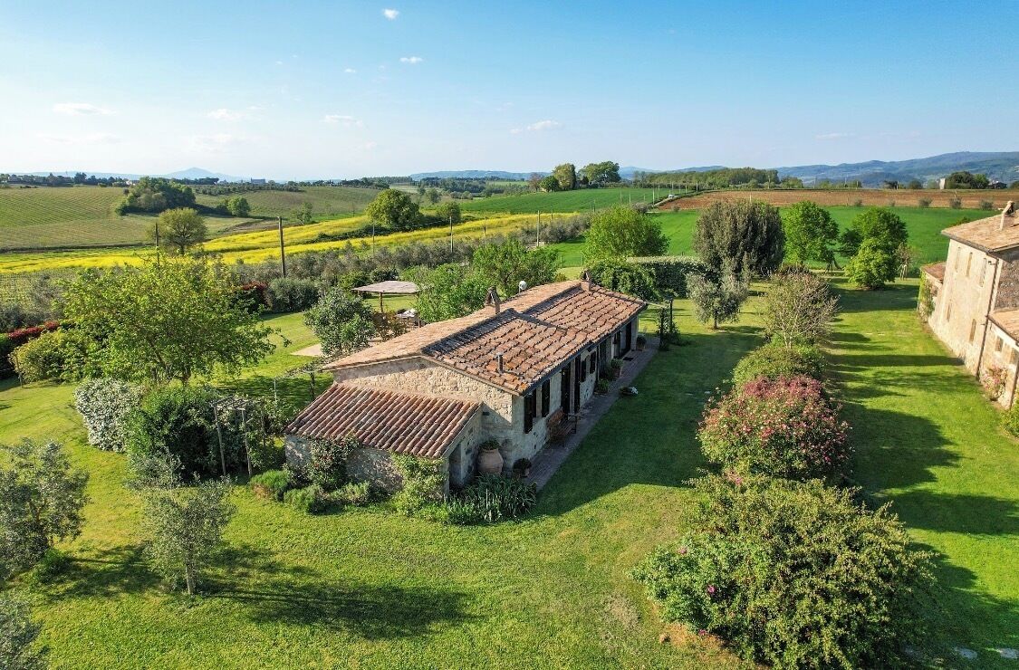 Une propriété rurale avec un bâtiment en pierre, un jardin et des champs en arrière-plan.