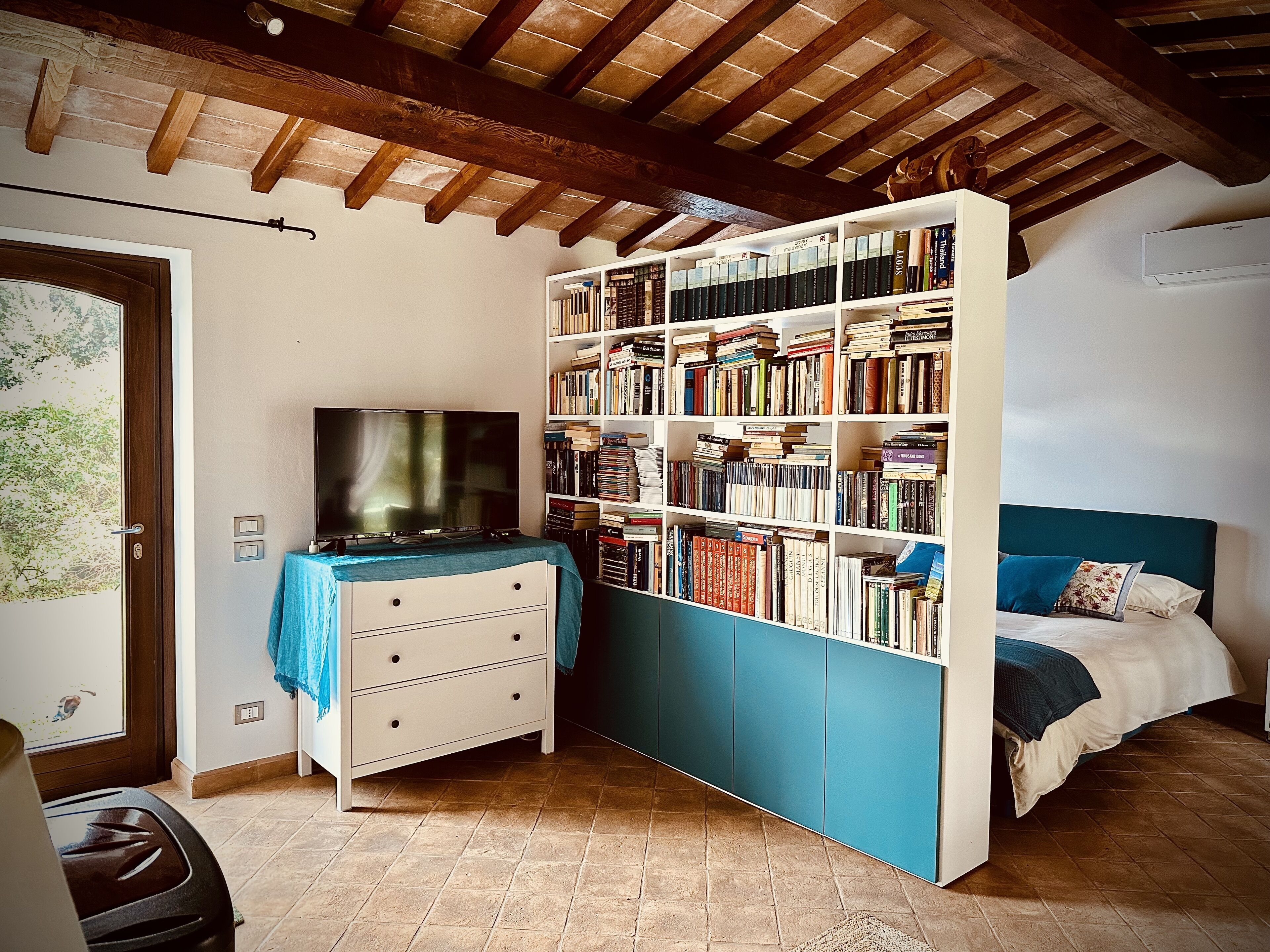 Een slaapkamer met een grote boekenkast, een televisie en een bed met blauw beddengoed.