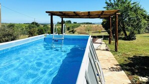 A rectangular swimming pool with clear blue water, surrounded by a tiled deck and a wooden pergola. - Milva's Nest Countryside (Umbria)