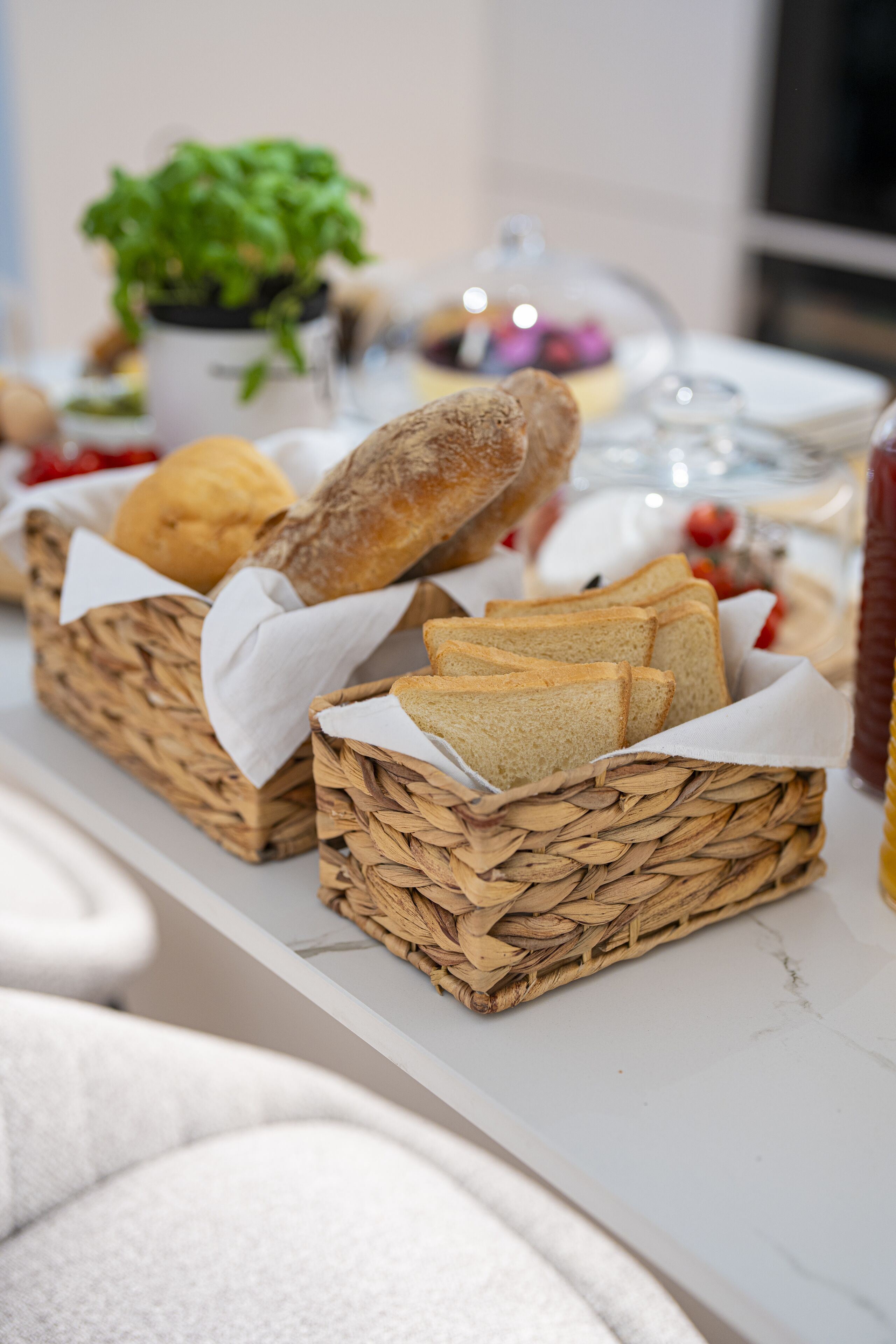Una mesa con cestas de pan y una planta en maceta al fondo.