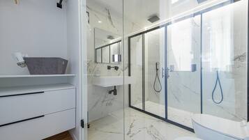 Un baño moderno con ducha de vidrio, lavamanos blanco y tocador con cajones.