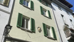 Un edificio de varios pisos con contraventanas verdes, un balcón visible y un cielo azul despejado.