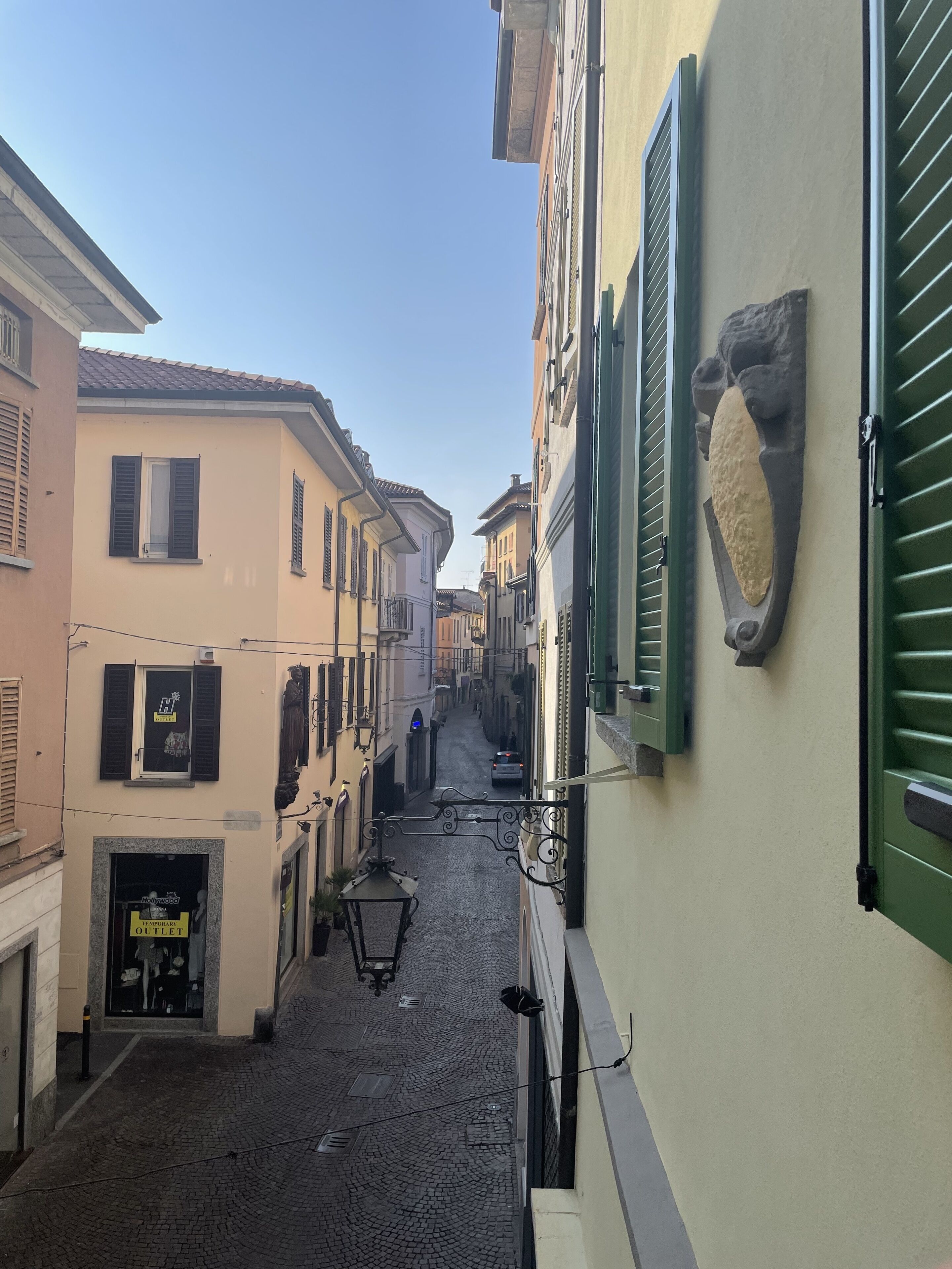 Una stretta strada acciottolata fiancheggiata da edifici con persiane e un rilievo in pietra su una parete.