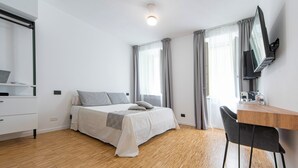 Un dormitorio con cama, escritorio, silla, televisor y ventana con cortinas.