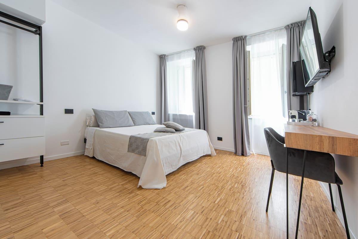 Une chambre à coucher comprenant un lit, un bureau, une chaise, un téléviseur et une fenêtre avec des rideaux.
