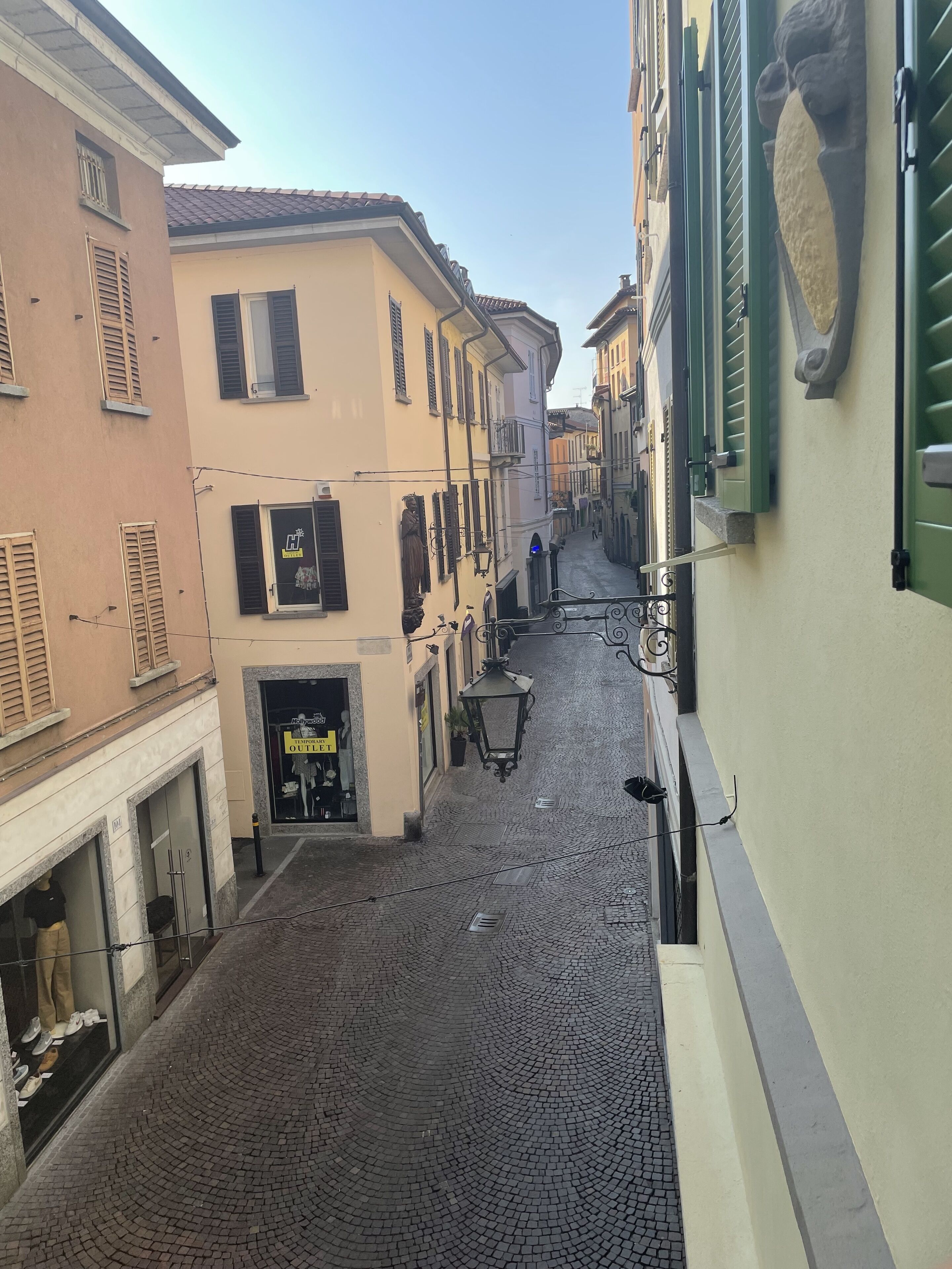 A narrow cobblestone street lined with buildings featuring traditional shutters and a storefront with mannequins.