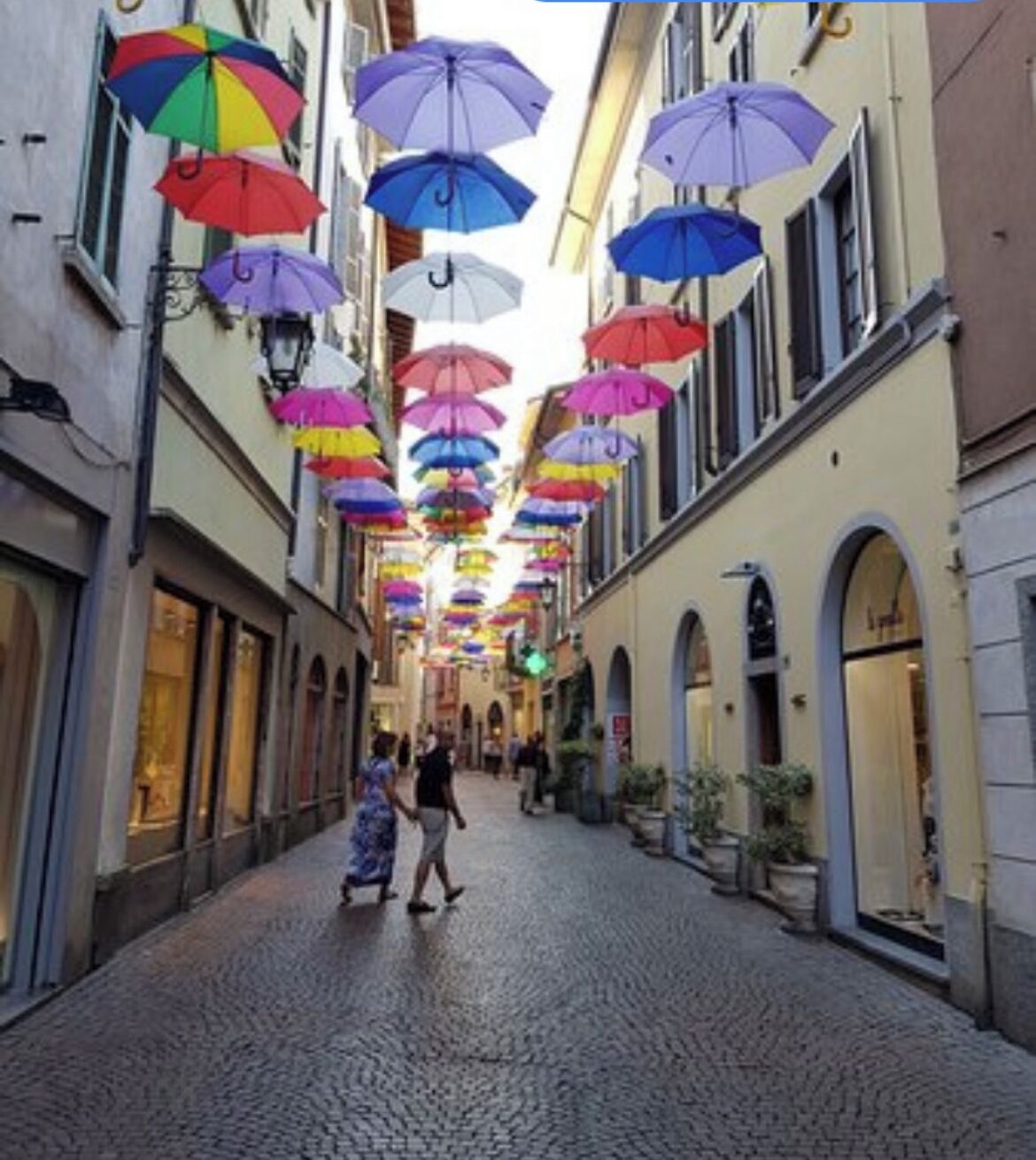 A cobblestone street with colorful umbrellas hanging overhead.