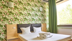 A hotel room with a bed, two pillows, a nightstand, a lamp, and a window with curtains. - Hotel Alma (Constanta)