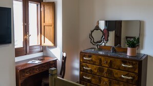 A room with a wooden desk, a dresser with drawers, a mirror, and a window with wooden shutters.