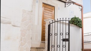 A white building with a stone facade, a wooden door, and a metal gate.