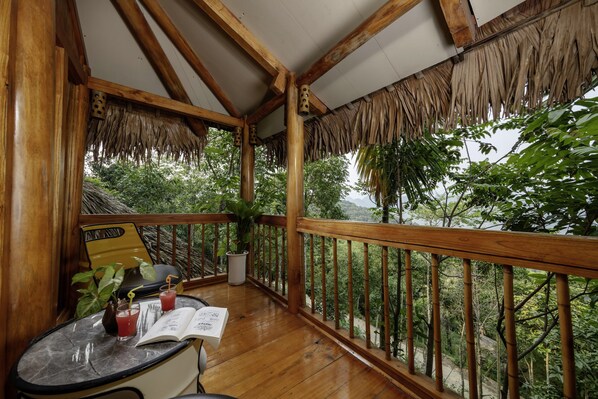 A wooden deck with a thatched roof, a table with drinks and a menu, and a view of lush greenery. - Gateway Inn Puluong (Hac Thanh)