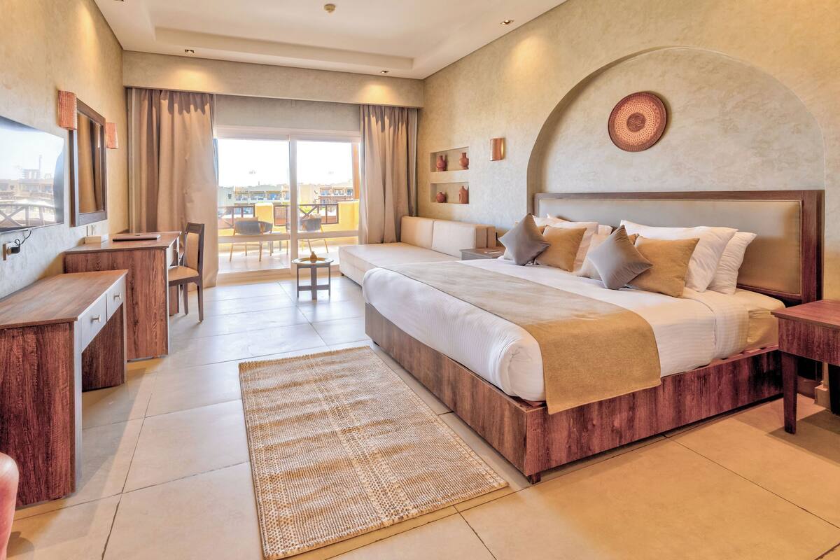 A modern hotel room with a large bed, a desk, and a balcony with a view.
