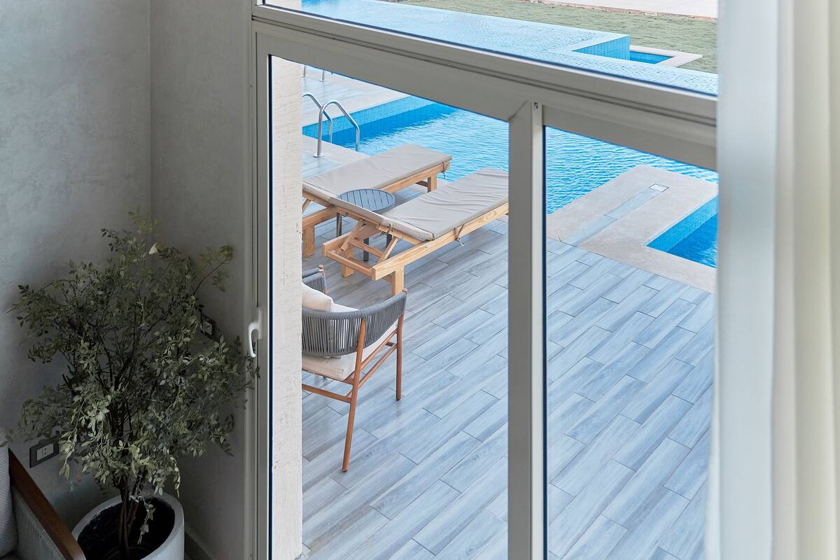 A view of a swimming pool area with a wooden deck, lounge chairs, and a potted plant.