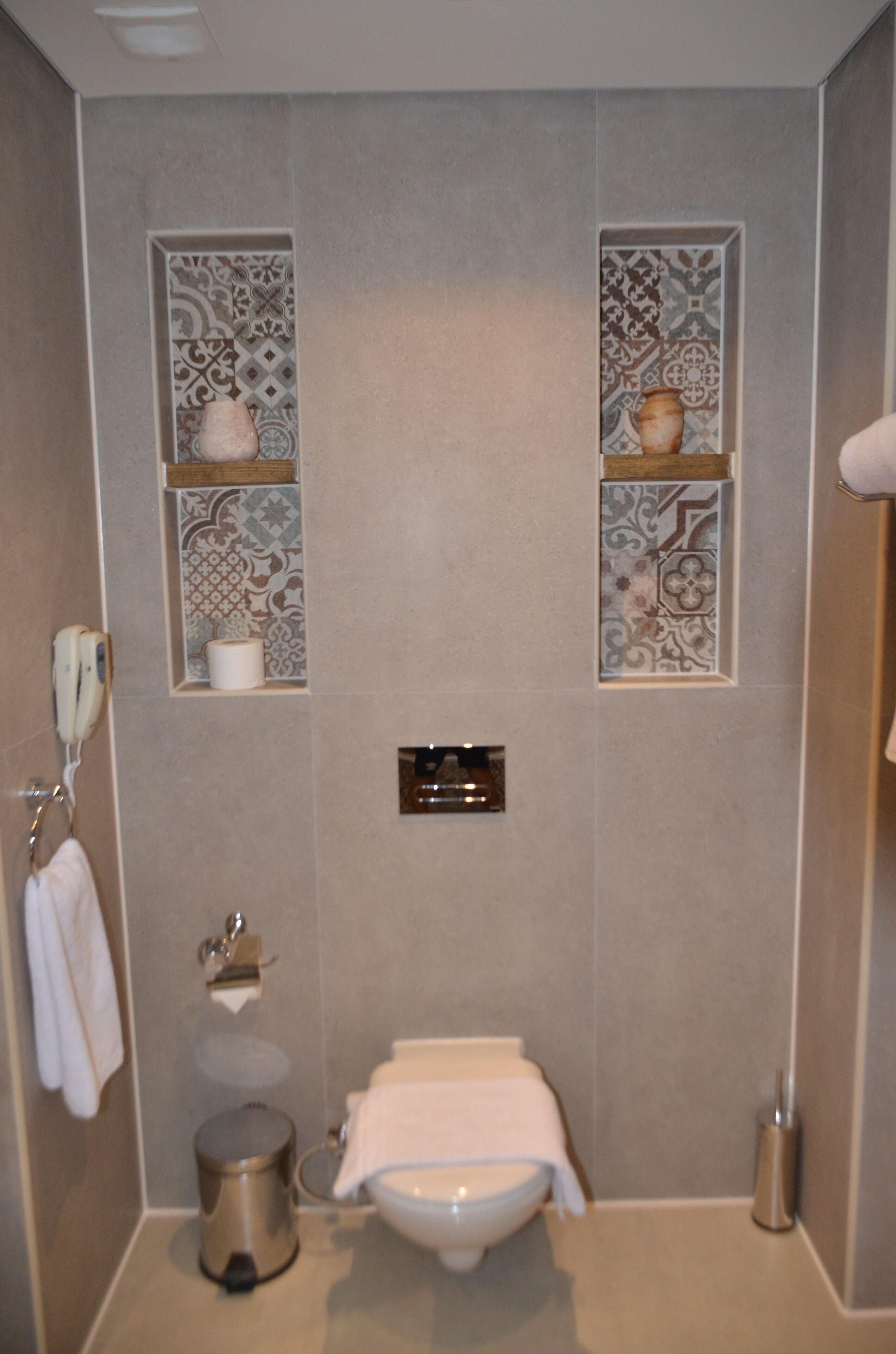 A bathroom with a toilet, a trash bin, a towel rack, and decorative tiles on the walls.