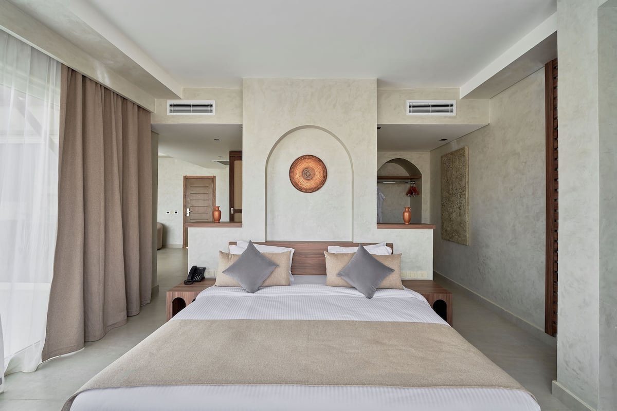 A modern hotel room with a large bed, two nightstands, a mirror, and a view of the hallway.