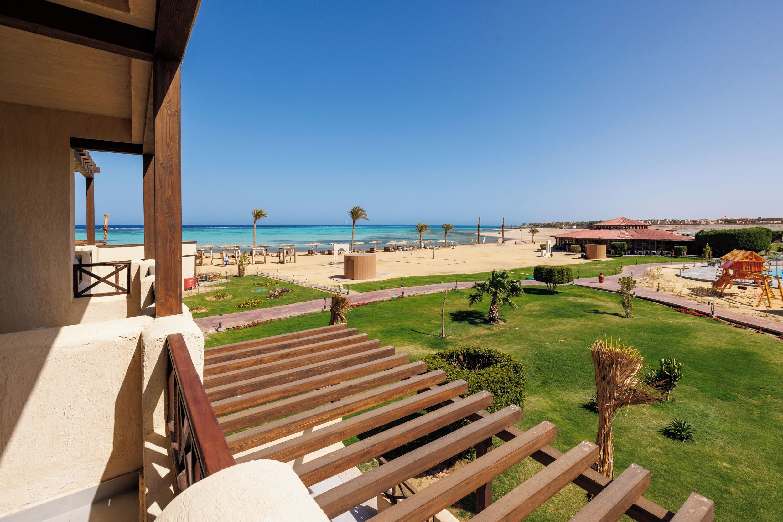 Un balcon doté de balustrades en bois, donnant sur une plage bordée de palmiers et surplombant un ciel bleu azur.
