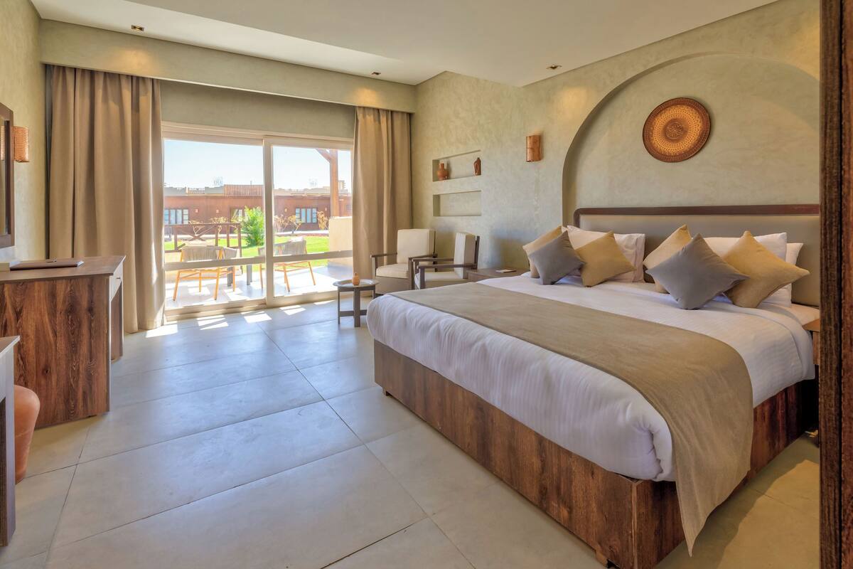 A spacious bedroom with a large bed, a desk, and a view of the outdoor patio.
