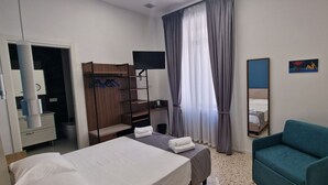 Quarto de hotel com cama, escrivaninha, cadeira, guarda-roupa e espelho.