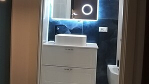 Um banheiro moderno com toucador, espelho com iluminação e parede de mármore escuro.