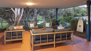 A covered patio area with two cushioned sofas and wicker chairs, a grill, and a surfboard. - Beach Retreat - Family & Pet Friendly + only 400m from beach (Quindalup)
