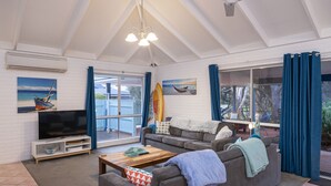 A spacious living room with a large flat-screen TV, grey sofas, a wooden coffee table, and artwork on the walls. - Beach Retreat - Family & Pet Friendly + only 400m from beach (Quindalup)