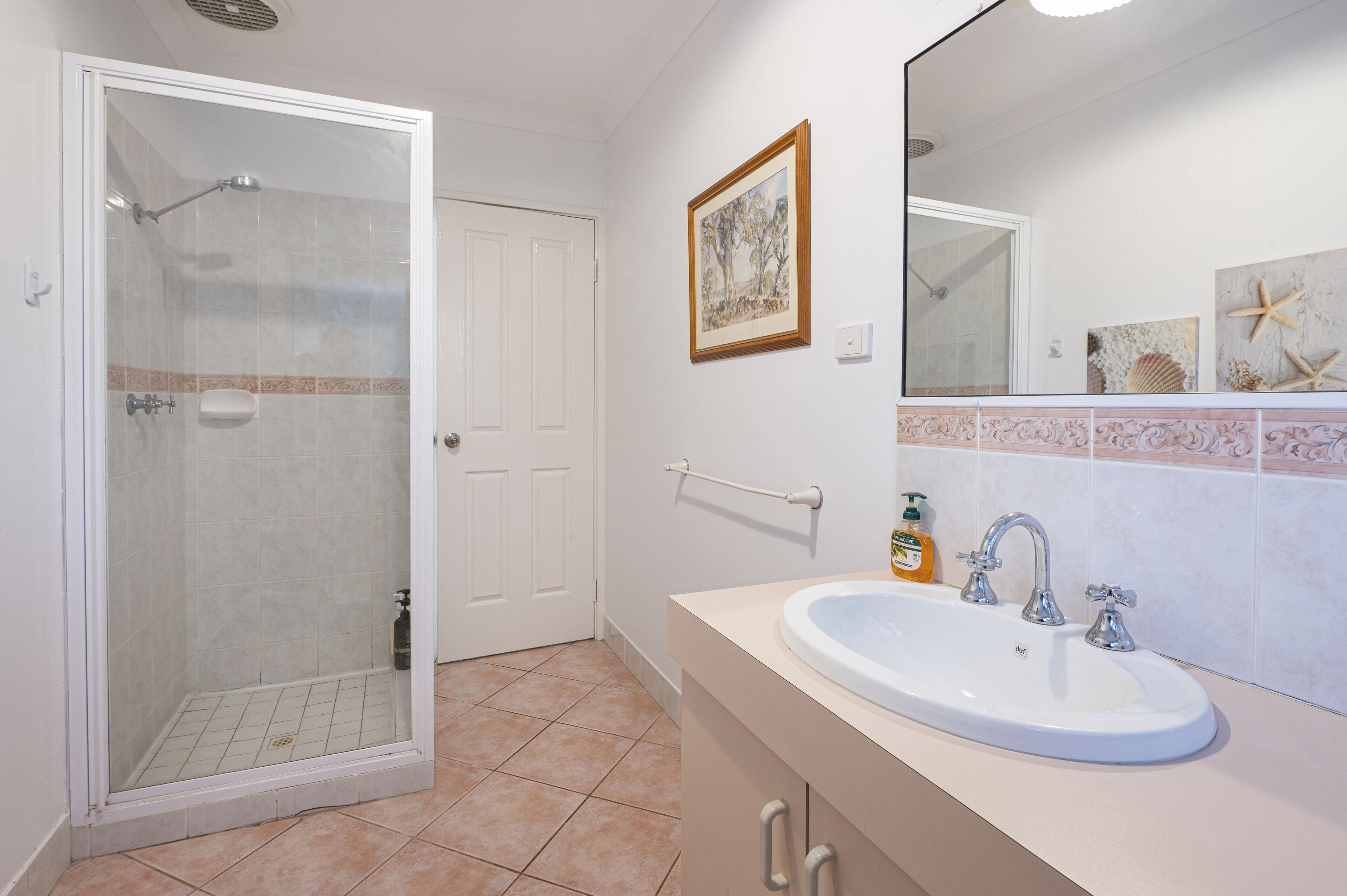 A bathroom with a glass-enclosed shower, a sink with two faucets, and a framed picture on the wall.