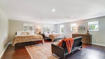 Een ruime slaapkamer met twee bedden, een slaapbank, een dressoir en een groot raam dat voor veel daglicht zorgt.