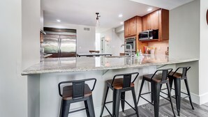 Una cocina moderna con una isla grande, taburetes de bar y electrodomésticos de acero inoxidable.