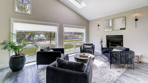 Un salón amplio con ventanas grandes, chimenea y muebles modernos.