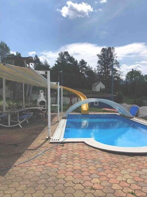 Relax by the pool surrounded by a patio with tables and chairs, and enjoy a fun slide into the water.