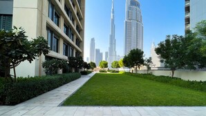 A modern urban landscape with high-rise buildings, a well-maintained grassy area, and a paved walkway.