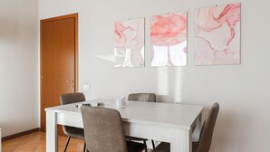 Un comedor con una mesa blanca, cuatro sillas y tres obras de arte abstracto en la pared.
