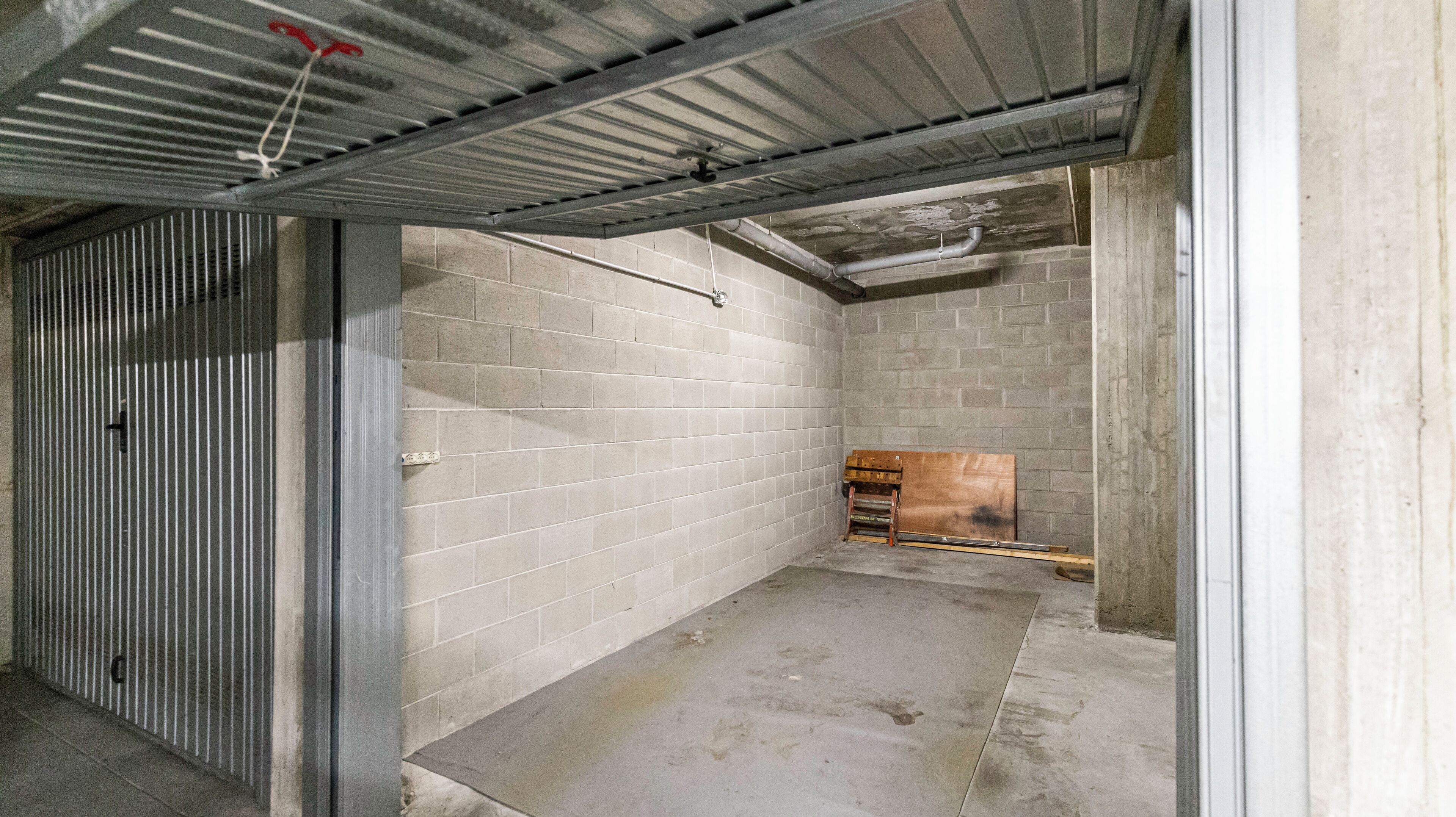 A concrete-walled, unfinished basement with a metal roof and exposed pipes.