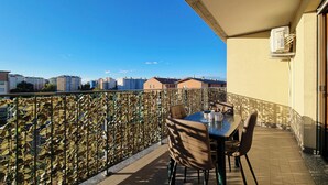 Un balcón con mesa y sillas, una valla decorativa y vistas a edificios al fondo.