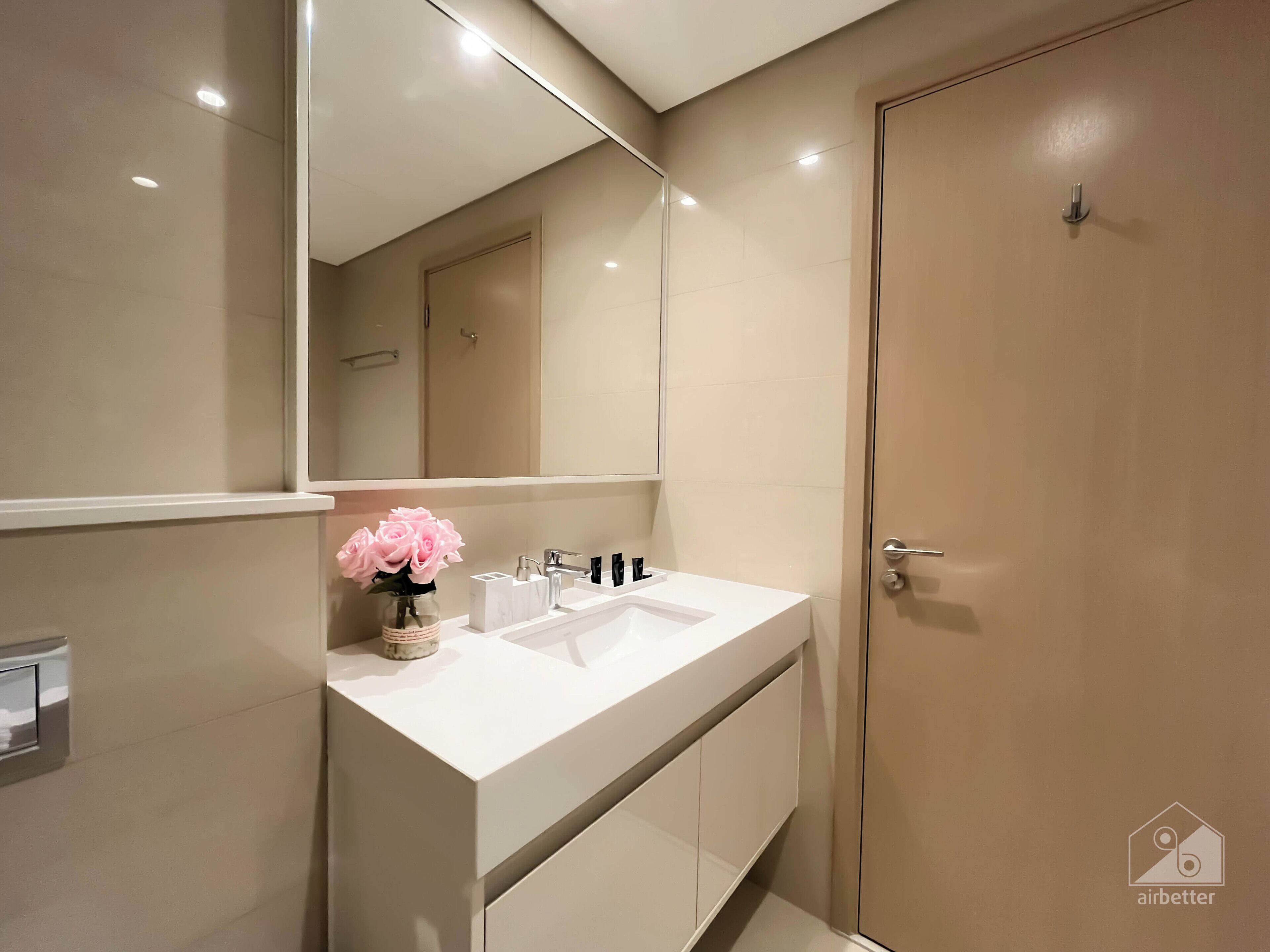 A modern bathroom with a white vanity, a large mirror, and a door.