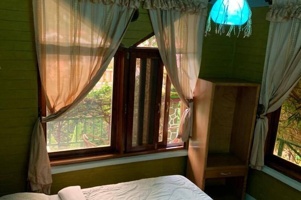 A bedroom with a bed, a window with curtains, and a ceiling with a unique pattern.