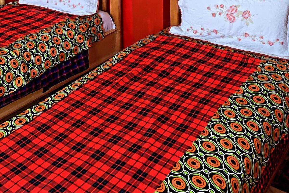 A hotel room with two beds, each with a red and black checkered bedspread, white pillows with floral patterns, and a red and white wall. The walls are adorned with framed artwork depicting various scenes and figures.