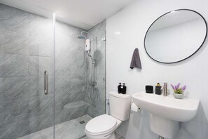 Ein modernes Badezimmer mit einer Duschkabine, einer Toilette, einem Waschbecken mit Spiegel und Toilettenartikeln.