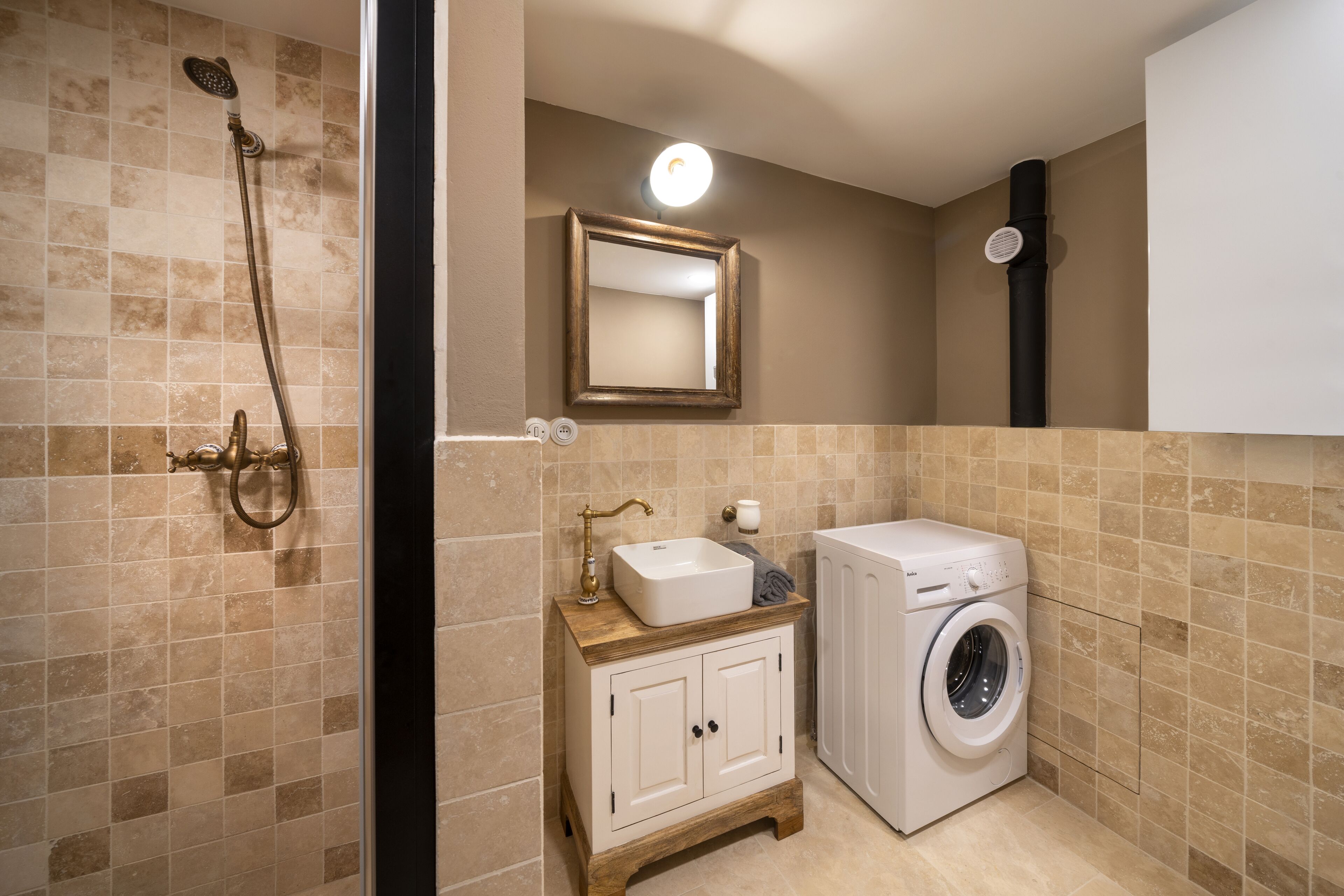 A bathroom with a shower, sink, mirror, and a washing machine.