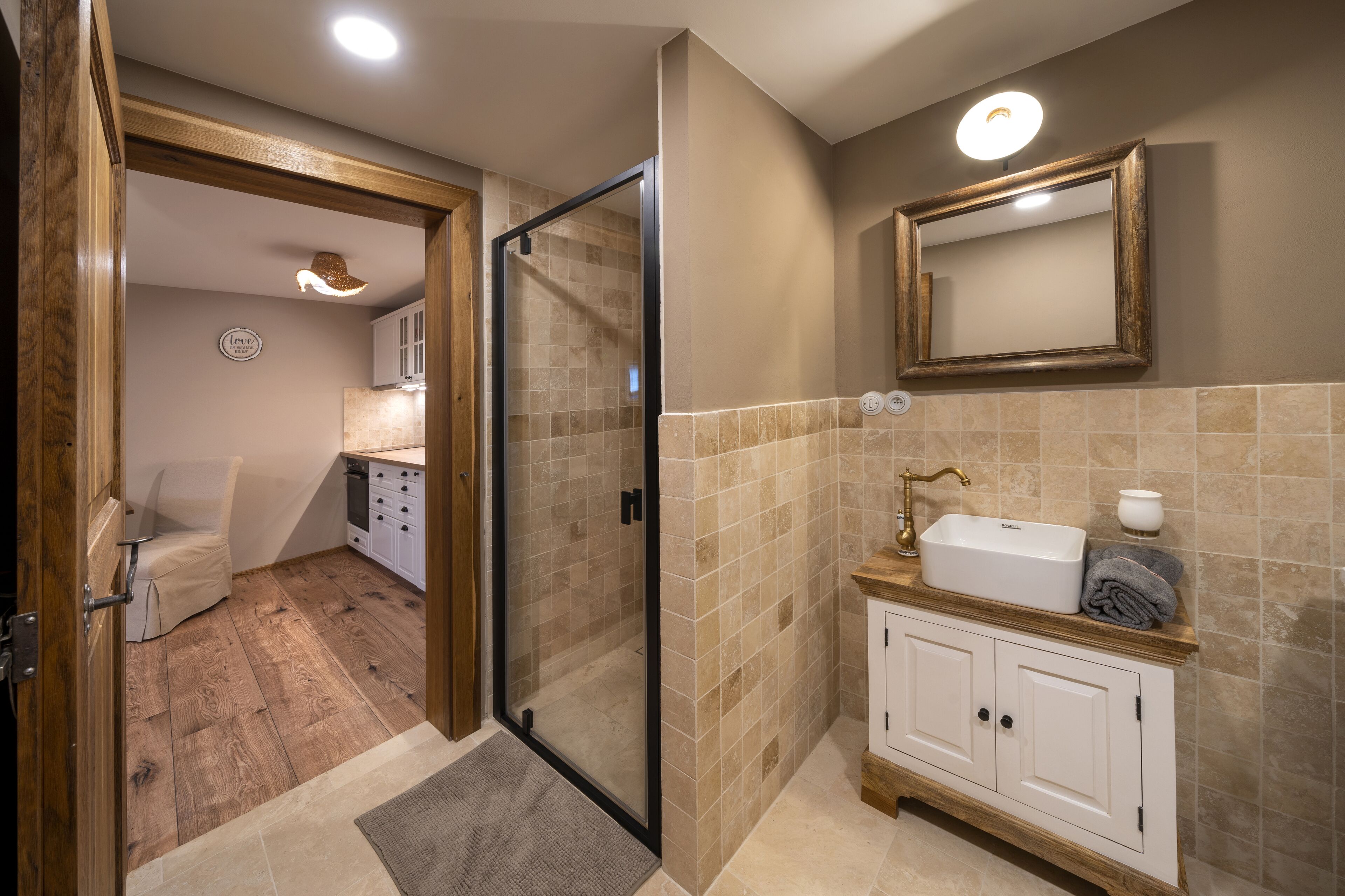 A modern bathroom with a glass shower enclosure, a wooden vanity, and a beige tiled backsplash.